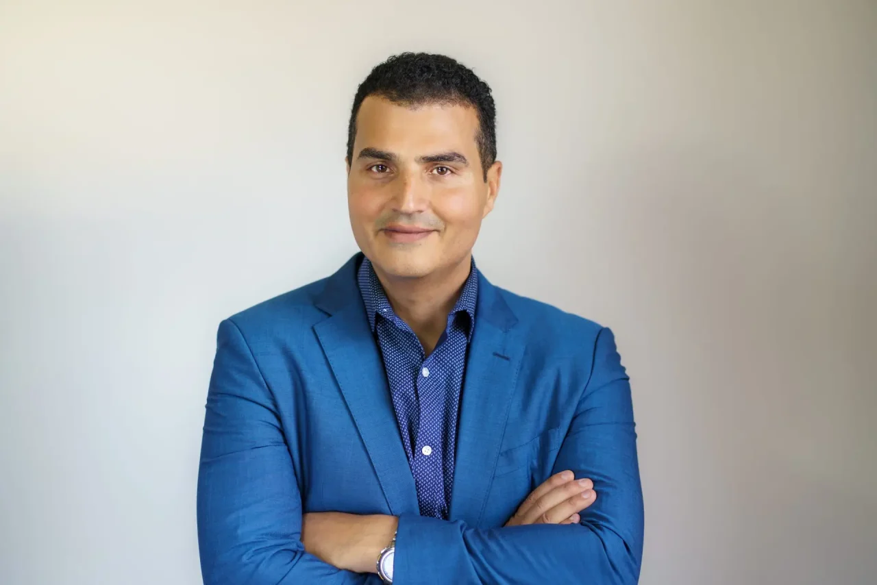 Loay Elbasyouni — primary portrait in a blue blazer. Photo: Erric Wright, July 2025.