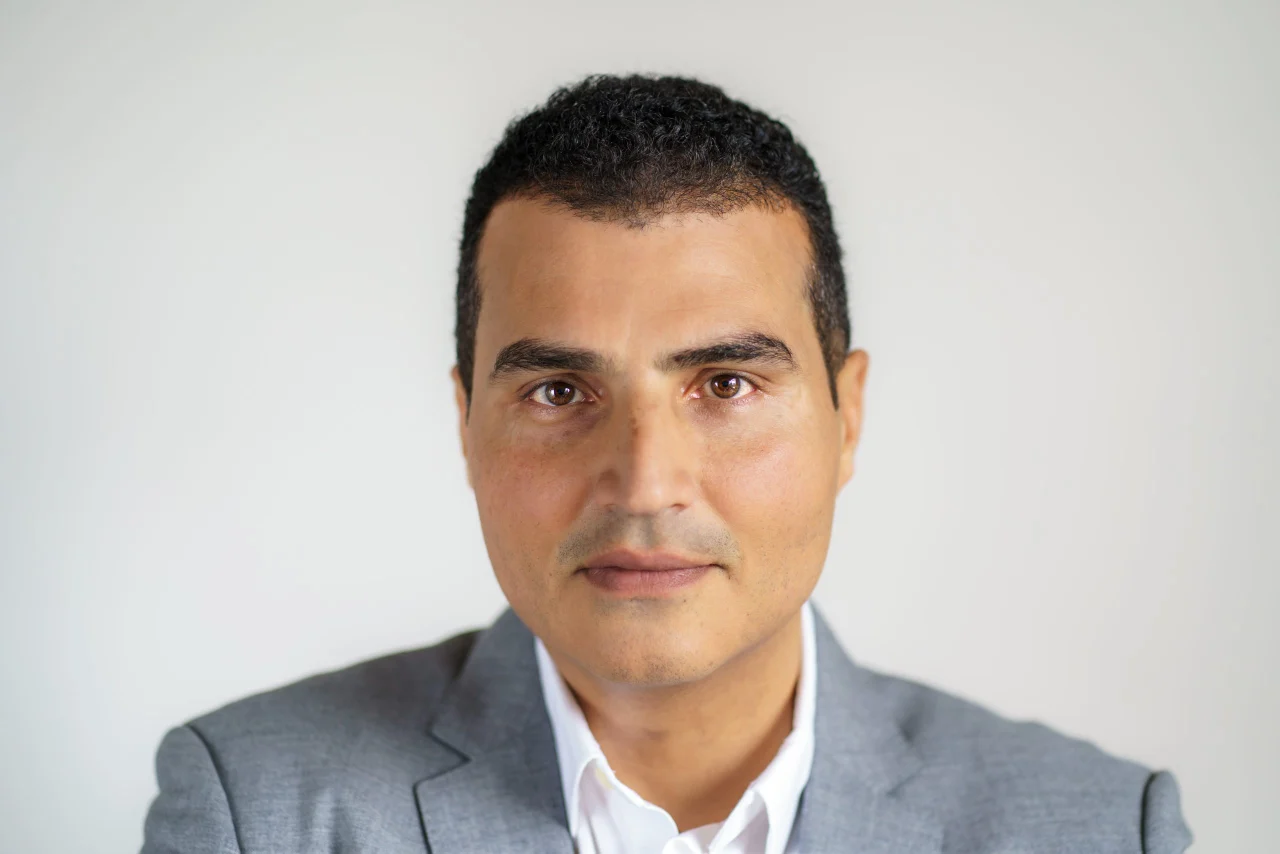 Loay Elbasyouni — classic headshot in a grey blazer. Photo: Erric Wright, July 2025.